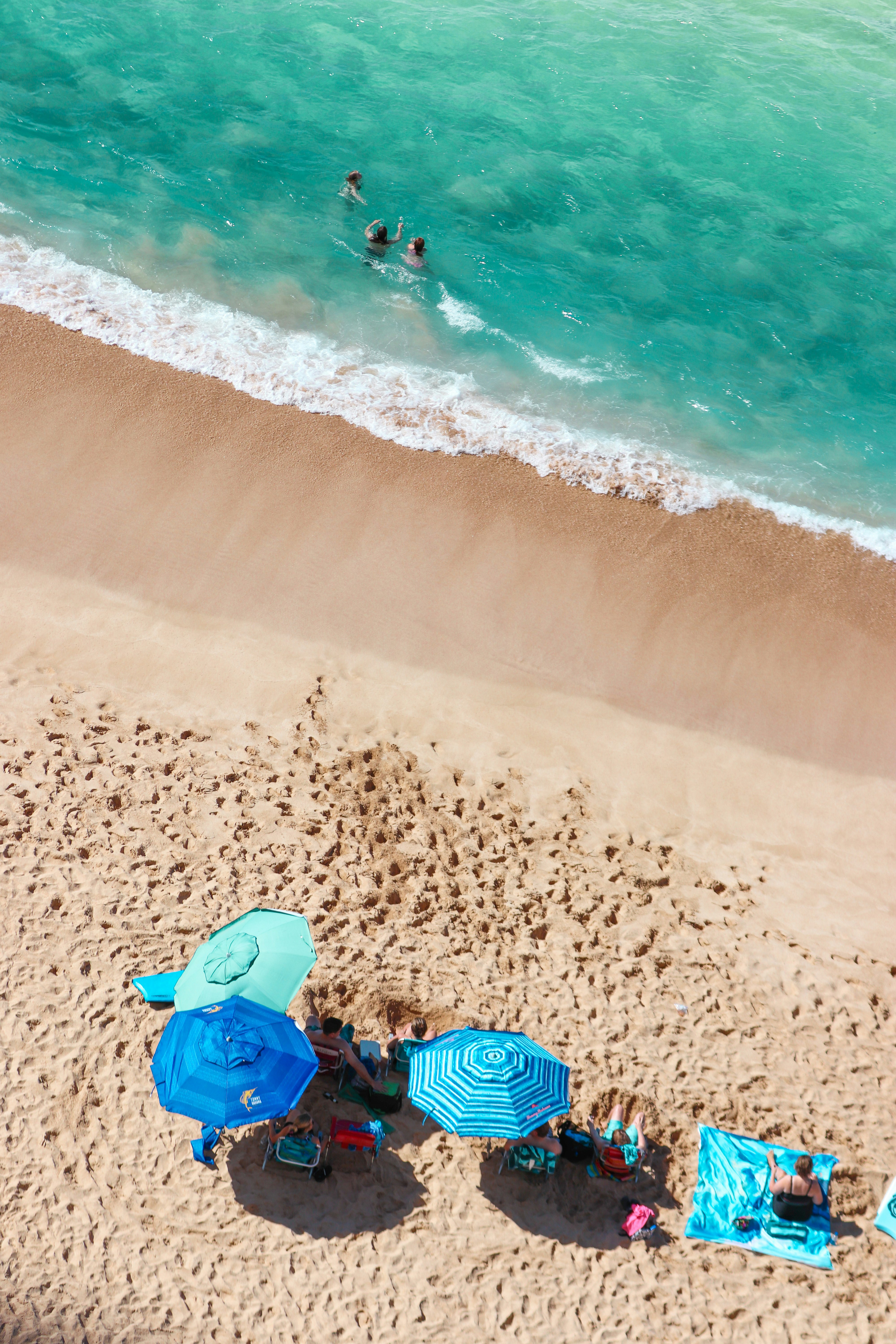 person in blue and green jacket sitting on beach shore during daytime